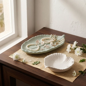 Leaf and shell shaped ceramic jewelry tray set on a vintage desk with pearl necklaces