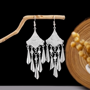 Detail of vintage silver-tone earrings with leaf fringe and heart charms on a wooden branch