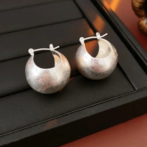 Detailed close-up of polished silver hoop earrings on a black textured jewelry display stand