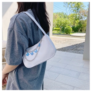 Detail of white shoulder bag with silver chain strap and blue butterfly pendant