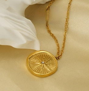 Macro view of gold 18k plated starburst pendant with crystal on satin background