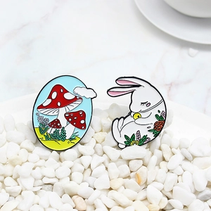 Cartoon enamel pin set featuring a red mushroom and white rabbit on white pebbles
