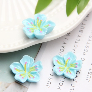 Three blue resin cherry blossom DIY accessories with yellow stamens on a white plate