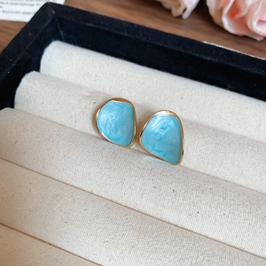 Macro shot of sky blue enamel tulip earrings with irregular gold trim in a jewelry box