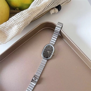 Detailed view of an oval silver quartz watch with a textured metal band in a tray