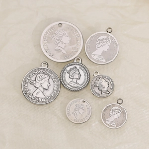 Set of silver stainless steel Elizabeth II coin pendants in various sizes on beige fabric