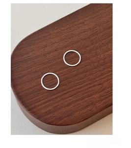 Detailed view of minimalist S999 sterling silver hoop earrings on a walnut wood stand