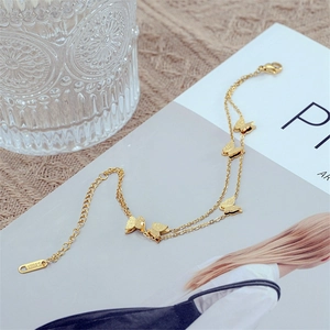 Double-layered golden stainless steel butterfly bracelet displayed on minimalist magazine