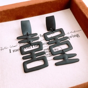 Detail of matte black Xi character stud earrings with tassels in a vintage jewelry box
