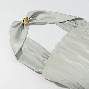 Detail eines seidenähnlichen salbeigrünen Kleides mit goldener Metallschnalle am Neckholder