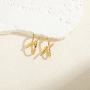 Detailed view of X-shaped gold earrings with micro-pave cubic zirconia on a stone surface