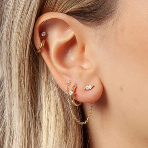 Close-up of gold chain fringe studs and eye-shaped crystal earrings on model ear