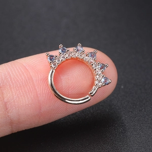 Close-up of rose gold crown ear hoop with blue and clear marquise zircons on finger