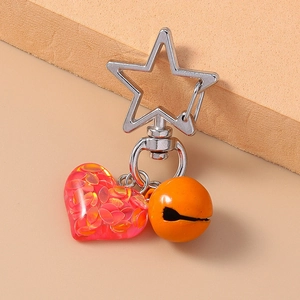 Detail of red resin heart pendant with sequins, silver star clasp, and orange bell