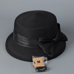 Dettaglio di cappello in paglia nera con nastro di raso, fiocco elegante ed etichetta taglia M