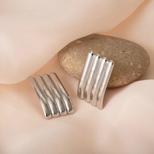 Close-up of silver ribbed tubular earrings on pink silk with decorative pebbles