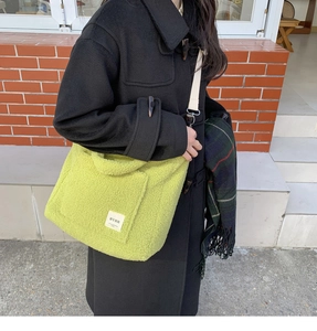Detail of lime green plush tote bag with logo patch worn with a black duffle coat
