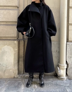 Détail d'un long trench-coat noir en laine avec un col montant haut et une coupe ample