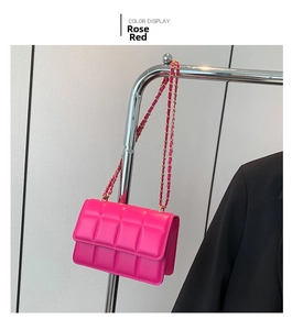 Detail of rose red quilted crossbody bag with golden chain strap on a metal display stand
