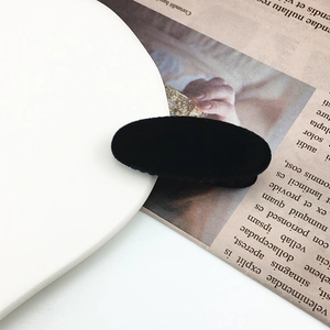 Detail shot of a black velvet oval hair clip on a newspaper background showing soft texture