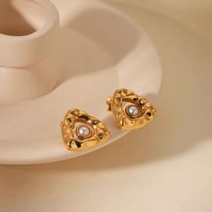 Detailed close-up of golden irregular heart earrings with pearls on ceramic prop