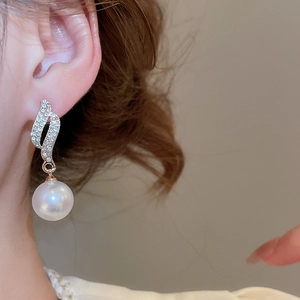 Close-up of a model wearing an elegant large white pearl earring with diamond-studded hook