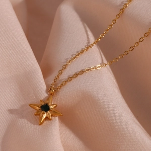 Makroaufnahme einer goldenen Stern-Halskette mit schwarzem Edelstein auf rosa Satin