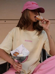 Dettaglio della stampa rosa ASSERTIVE su una t-shirt in cotone giallo pallido chic