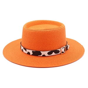 Detail of orange woven straw hat with cow print ribbon and stylish metal buckle