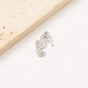 Macro shot of a silver seahorse pendant on a beige porous stone with a white background