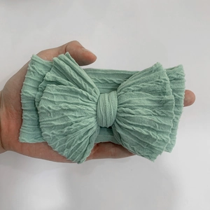 Detail showing hand holding a light green cable knit nylon bow headband for infants