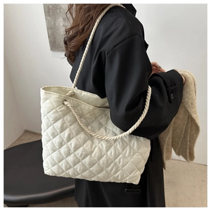 Détail du sac cabas matelassé crème avec bandoulières en corde sur un manteau noir