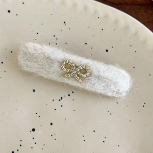 Detailed macro view of a white felt hair clip featuring a sparkling rhinestone bow