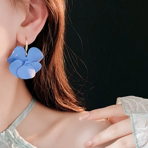 Macro detail of oversized blue floral earrings on model showing matte finish and scale