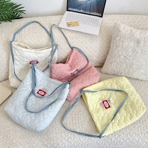 Flat lay of heart-quilted crossbody bags in four macaron colors on a soft plush rug