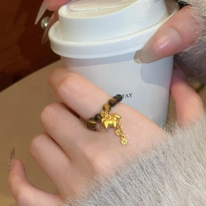 Detail of tiger eye bead ring with horse charm and coins worn on hand with coffee