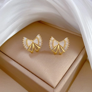 Detailed macro view of gold bow-knot earrings with white mother-of-pearl and zircon inlay