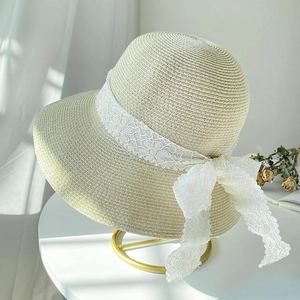 Chic beige straw sun hat with white lace bow decoration on a gold display stand