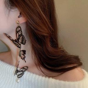 Détail de boucles d'oreilles papillon noires avec cristaux et une perle suspendue