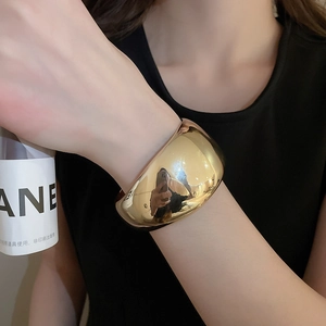 Gros plan d'un gros bracelet manchette doré en forme de haricot au fini poli miroir