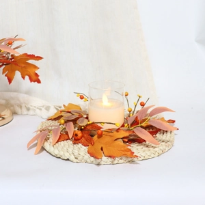 Detail of LED candle in glass cup with maple leaf and berry wreath on a woven mat