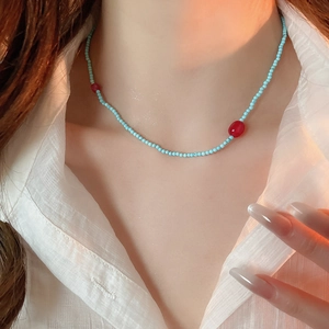 Close-up of blue beaded star necklace with red accents on model wearing white shirt