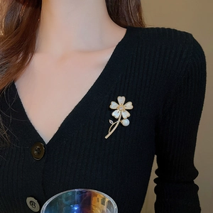 Détail de la broche papillon en or avec pétales en nacre et perle sur un tricot noir
