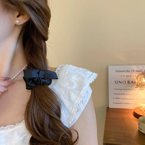Detail of a black satin oversized bow scrunchie styled on a brunette braided hairstyle
