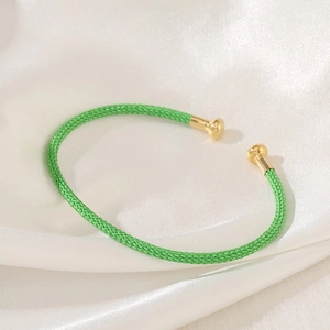 Detail showing green braided bracelet with polished gold-tone metal ball ends