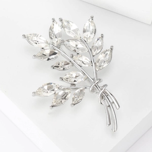 Macro detail of silver wheat ear brooch with marquise-cut crystals on white pedestal
