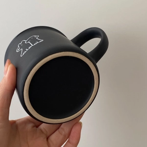 Taza minimalista de cerámica negra mate con dibujo de cachorro blanco en mano
