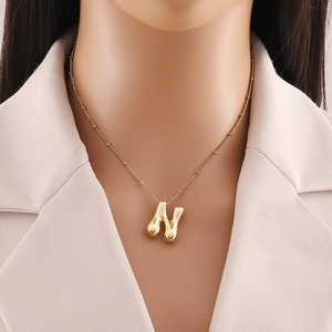 Dettaglio del ciondolo lettera N placcato oro 18K su catena a perline con blazer beige
