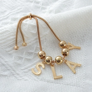 Macro shot of gold stainless steel bracelet featuring SLYA letter charms and sliding clasp