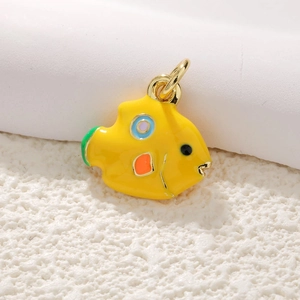 Macro shot of gold-plated fish pendant with colorful enamel dots on coral background